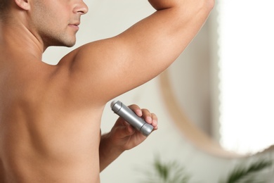 Photo of Young man applying deodorant to armpit indoors, closeup