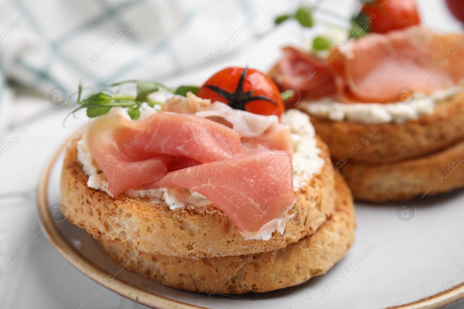 Photo of Tasty rusks with prosciutto, cream cheese and tomatoes served on white table, closeup