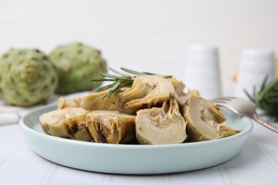 Photo of Plate with pickled artichokes and rosemary on white tiled table, closeup