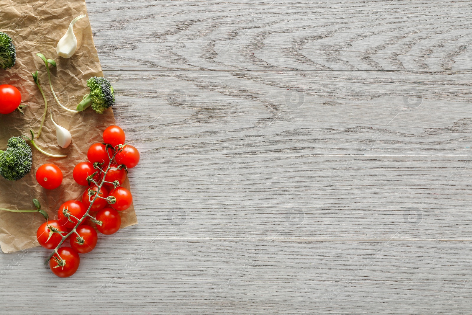 Photo of Food photography. Fresh cherry tomatoes, broccoli, garlic and microgreen on wooden table, flat lay with space for text