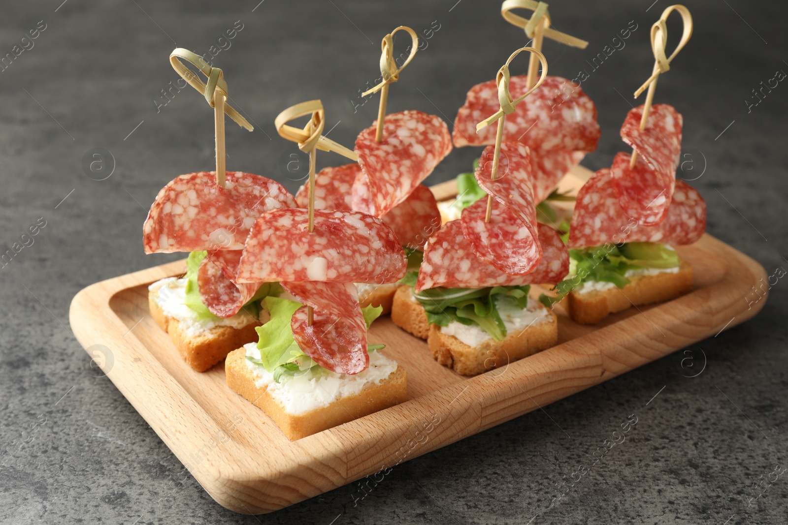 Photo of Tasty canapes with salami, greens and cream cheese on grey table