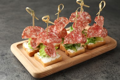 Photo of Tasty canapes with salami, greens and cream cheese on grey table