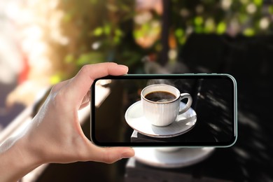 Image of Woman taking picture of hot aromatic coffee on table in outdoor cafe