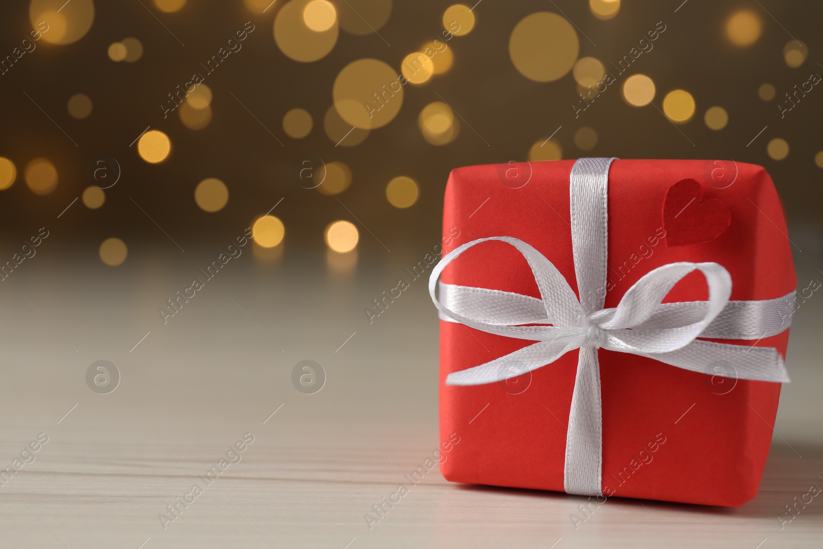 Photo of Beautiful gift box on wooden table against blurred lights, closeup. Space for text