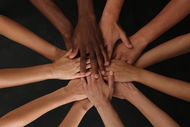 Photo of Group of multiracial people joining hands together on black background, closeup
