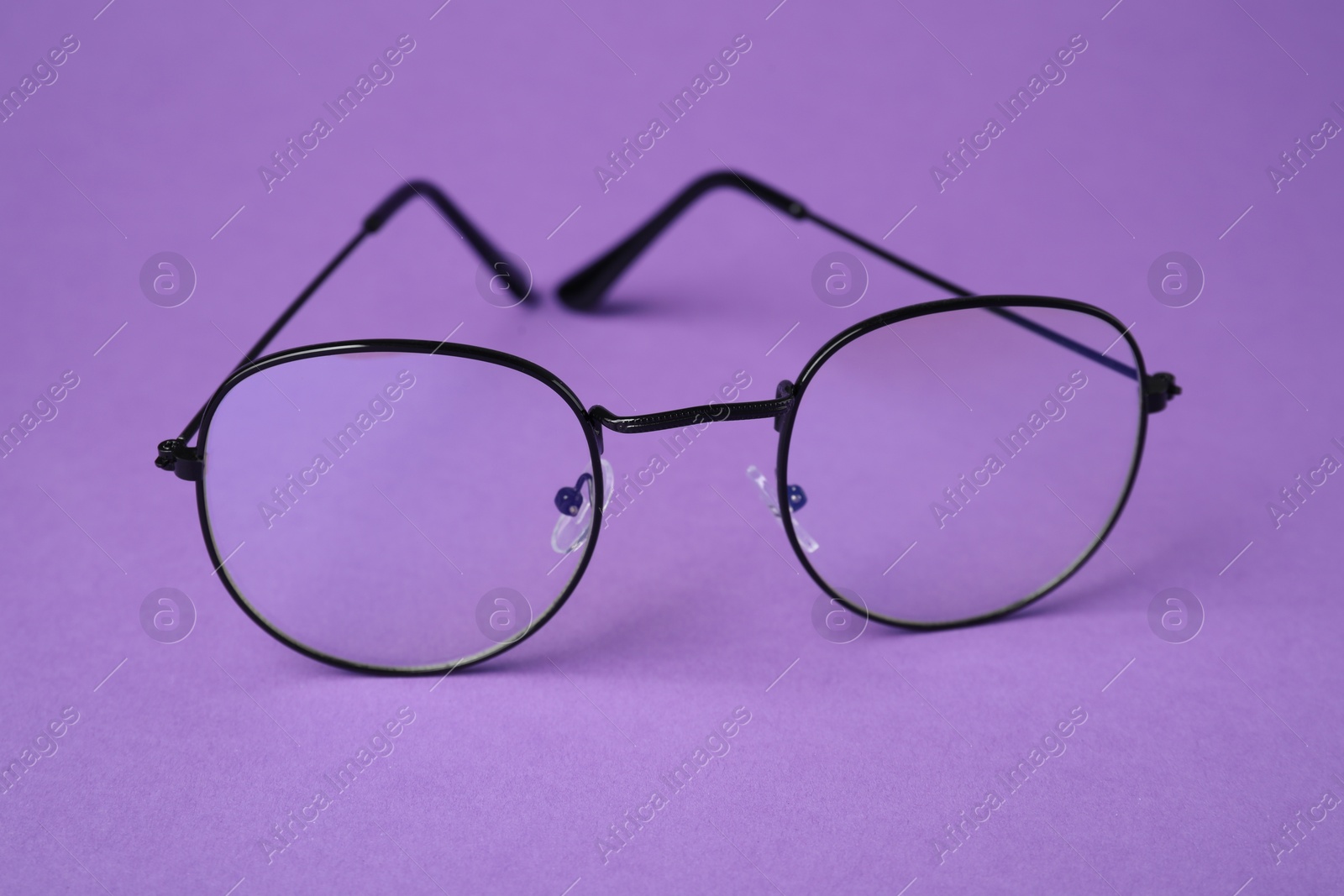 Photo of Stylish pair of glasses with black frame on purple background, closeup