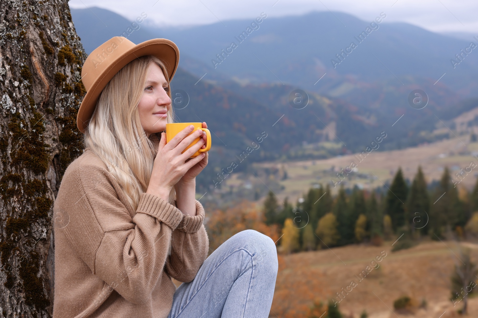 Photo of Young woman with mug of hot drink in mountains. Space for text