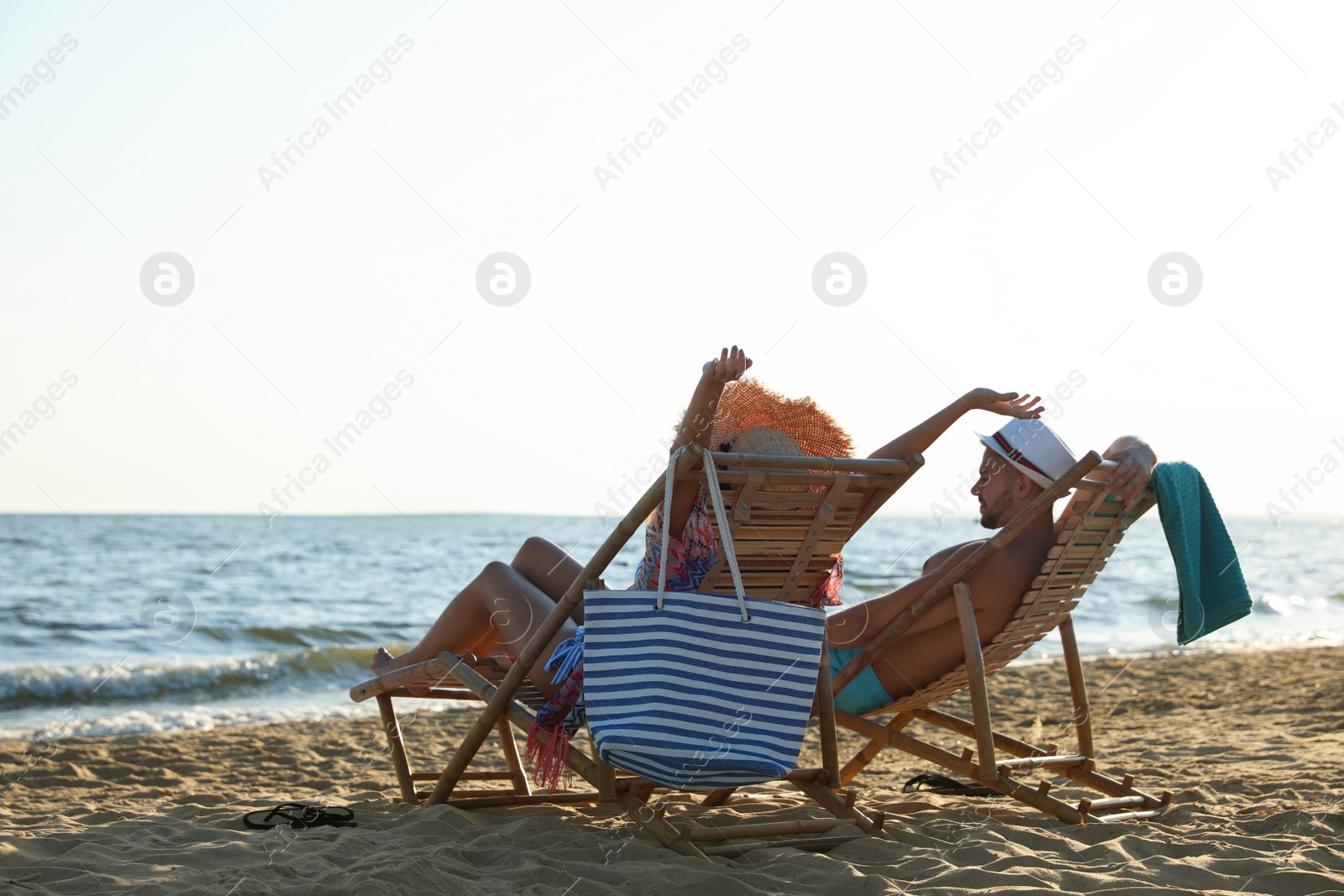 Photo of Young couple relaxing in deck chairs on beach near sea