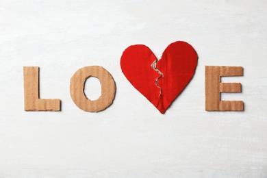 Photo of Word "Love" with torn cardboard heart and letters on light background, top view. Relationship problems