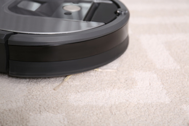 Photo of Hoovering floor with modern robotic vacuum cleaner indoors, closeup