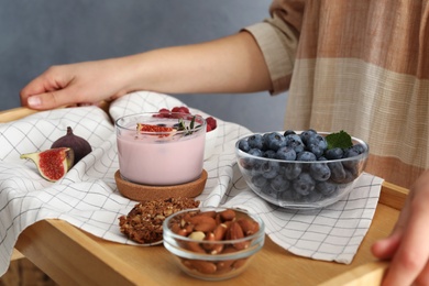 Woman holding wooden tray with delicious breakfast and fig smoothie, closeup