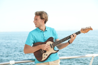 Photo of Portrait of handsome young man with guitar on sea pier