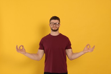 Photo of Young man meditating on orange background. Zen concept