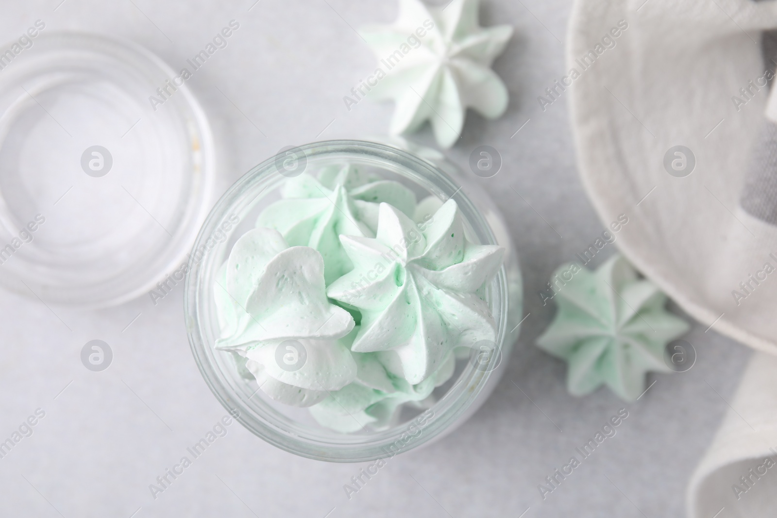 Photo of Tasty meringue cookies in glass jar on light grey table, top view