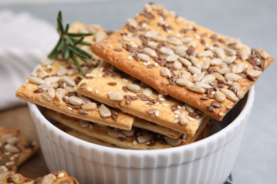 Photo of Cereal crackers with flax, sunflower and sesame seeds in bowl on grey table, closeup