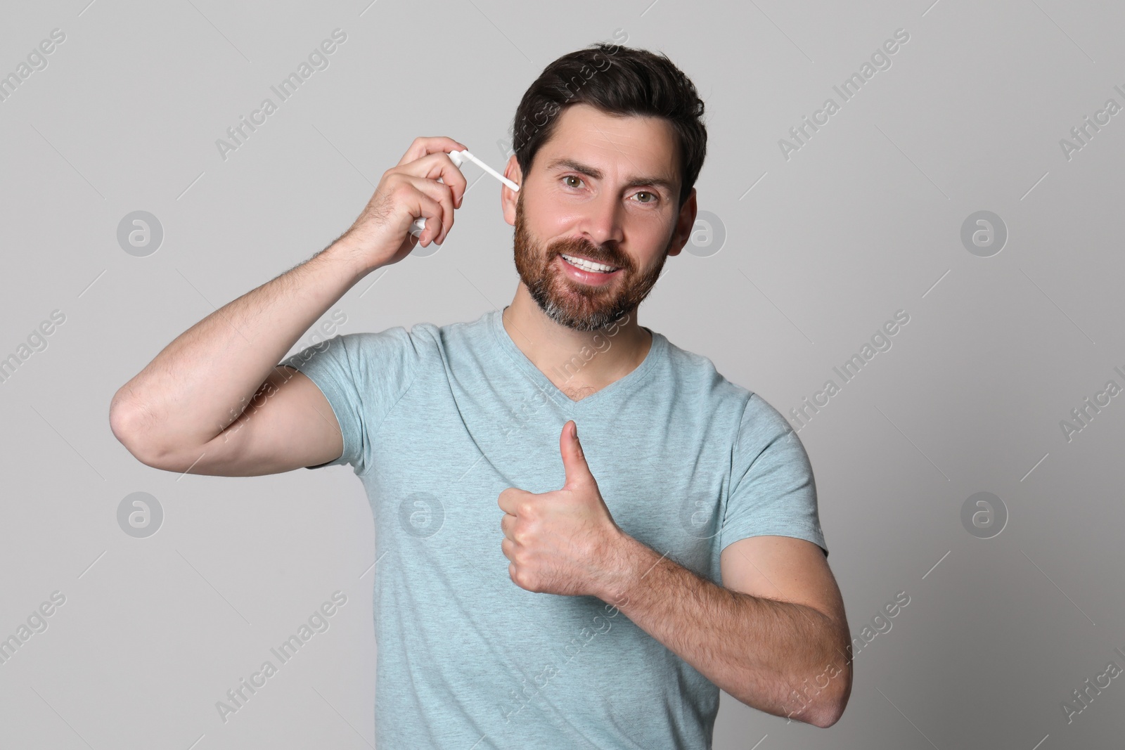 Photo of Man using ear spray and showing thumbs up on grey background
