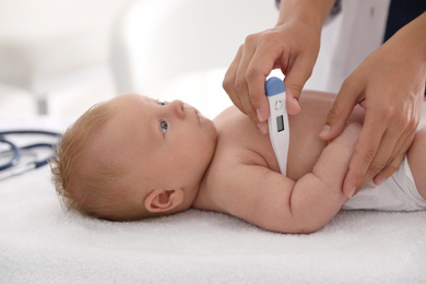 Photo of Doctor measuring temperature of little baby with digital thermometer indoors, closeup. Health care