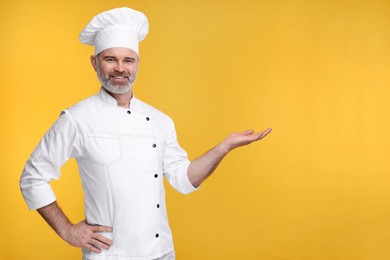Photo of Happy chef in uniform showing something on orange background, space for text