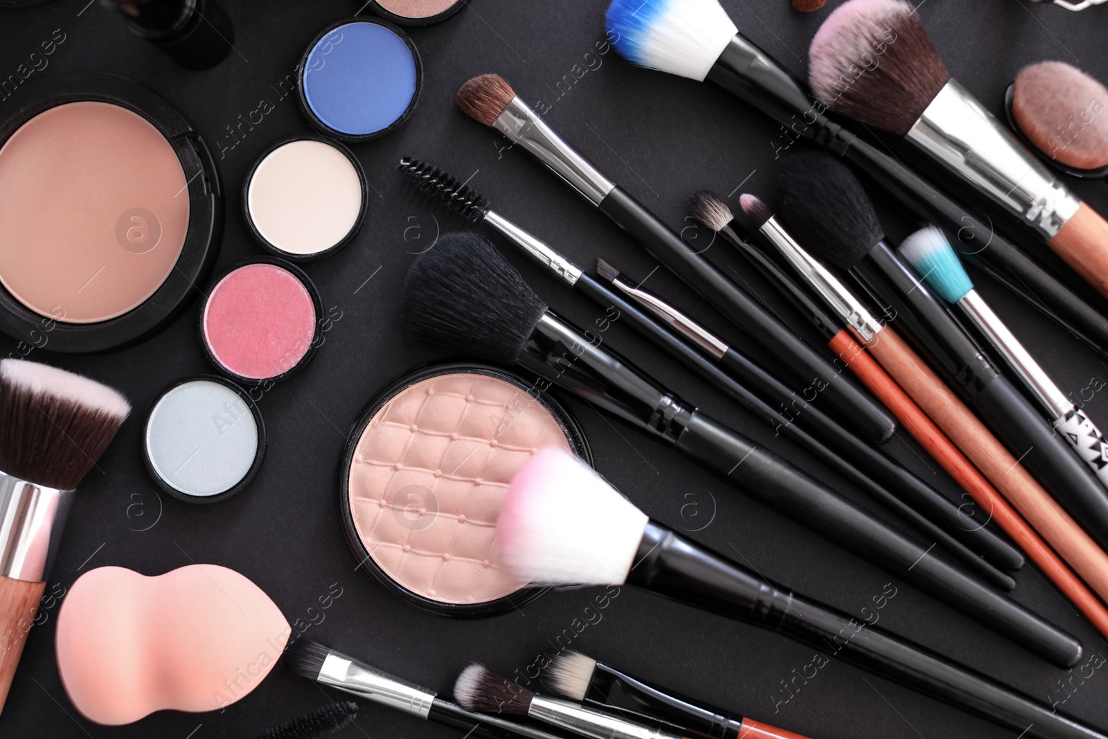 Photo of Flat lay composition with makeup brushes and cosmetic products on black background