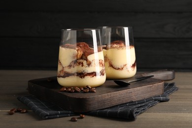 Photo of Delicious tiramisu in glasses, spoon and coffee beans on wooden table