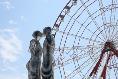 Photo of BATUMI, GEORGIA - JUNE 14, 2022: Movable sculptural composition Ali and Nino near Ferris wheel, low angle view