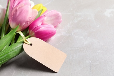 Photo of Beautiful tulips and blank label on marble background, space for text. International Women's Day