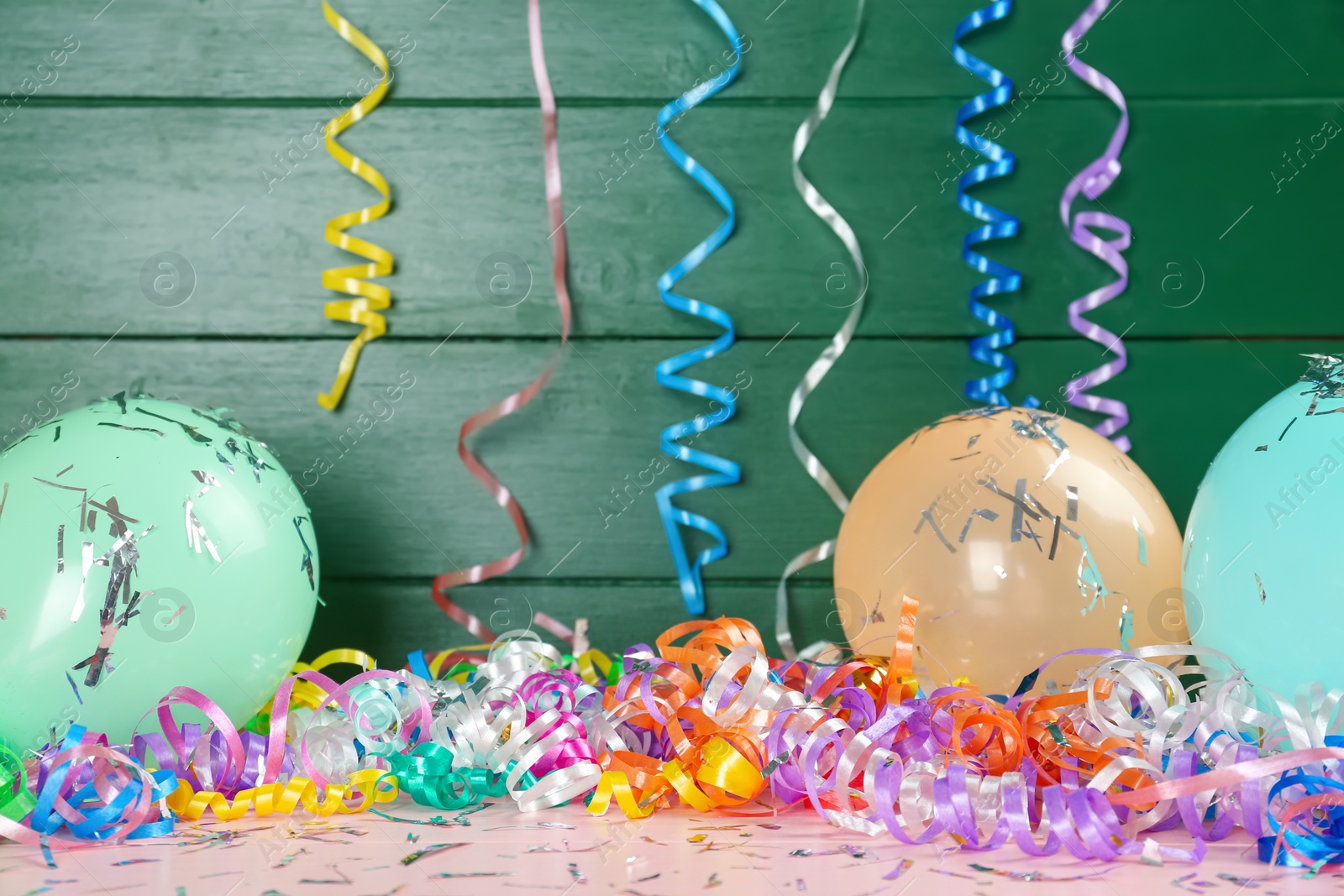 Photo of Colorful serpentine streamers, balloons and confetti on pink wooden table