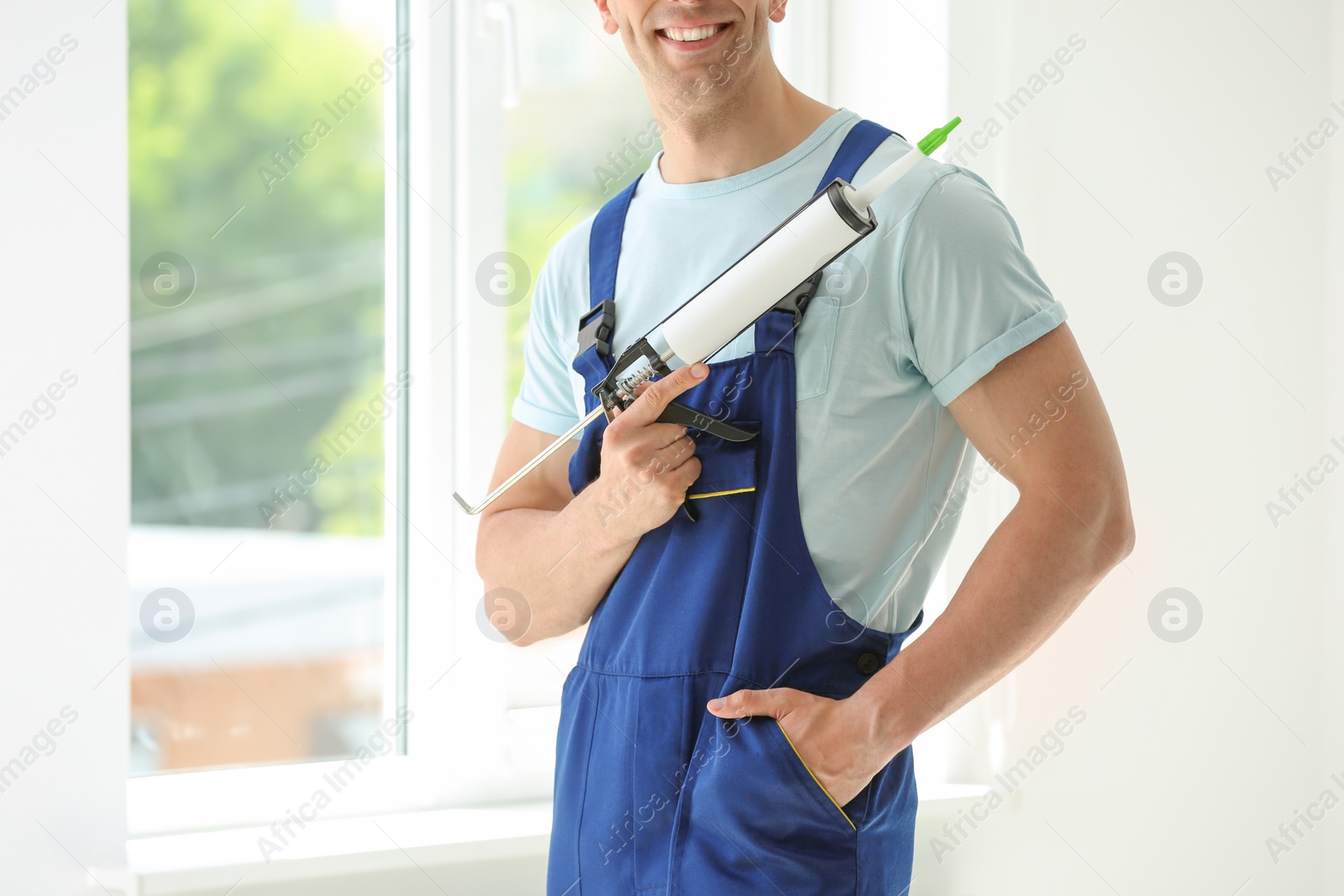 Photo of Construction worker in uniform with window sealant indoors