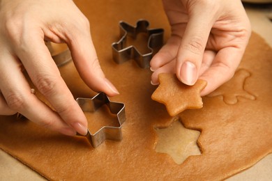 Photo of Woman cutting dough with cookie cutter at table, closeup