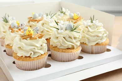 Photo of Tasty Easter cupcakes with vanilla cream in box on table, closeup