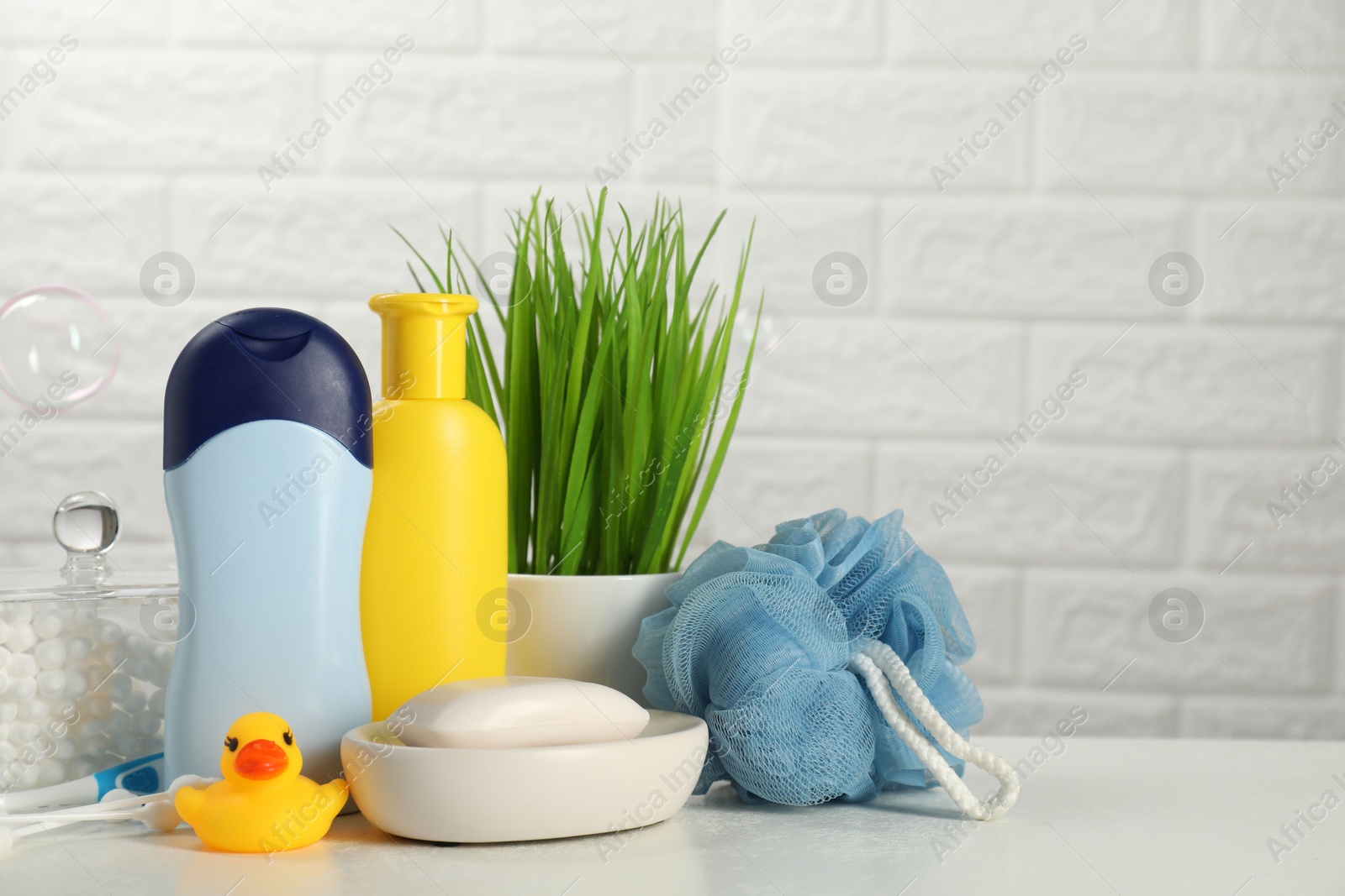 Photo of Different baby bath accessories and cosmetic products on white table against brick wall