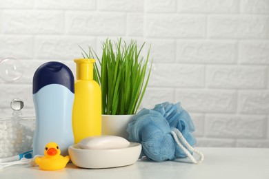 Photo of Different baby bath accessories and cosmetic products on white table against brick wall