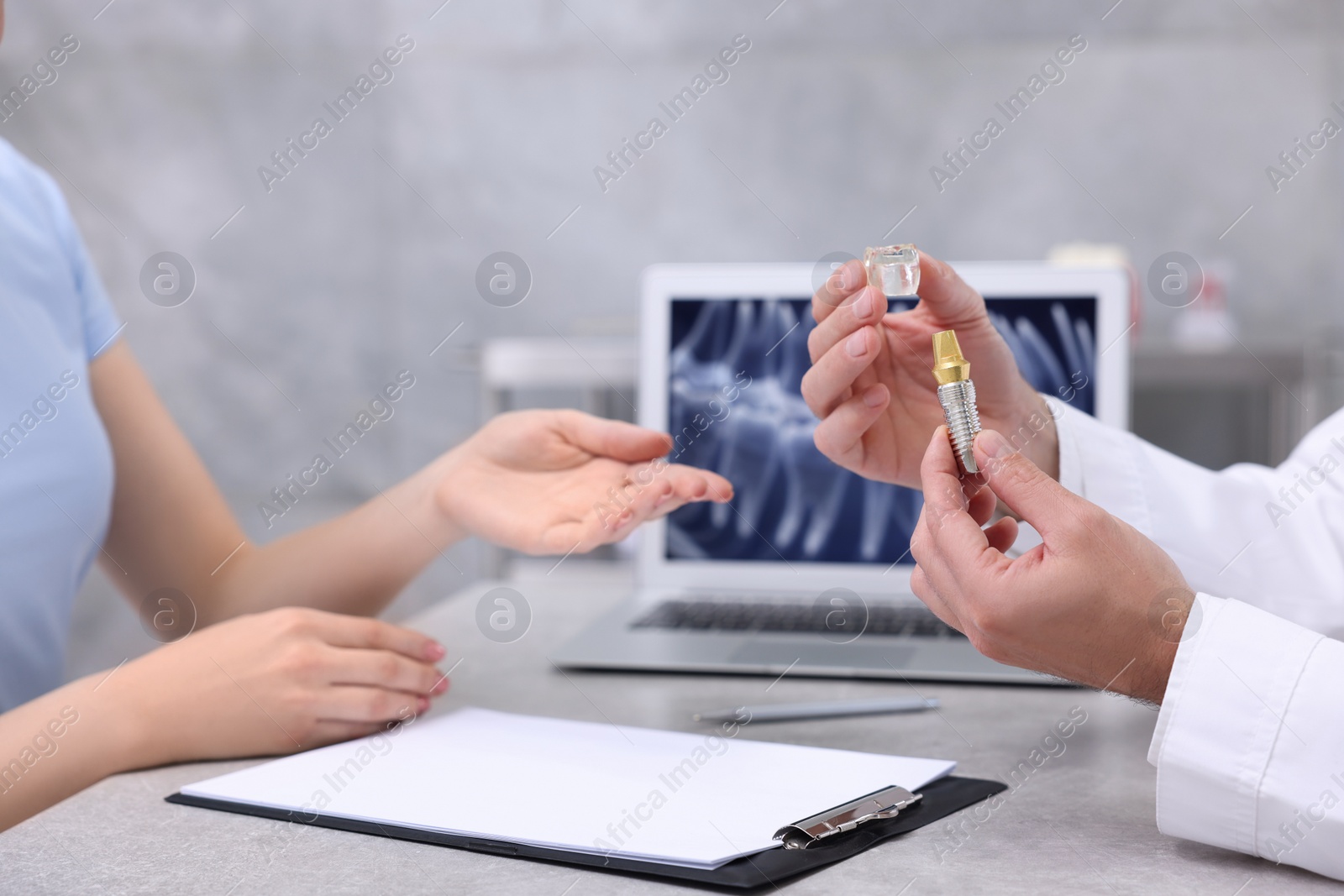 Photo of Doctor showing patient educational model of dental implant in clinic, closeup