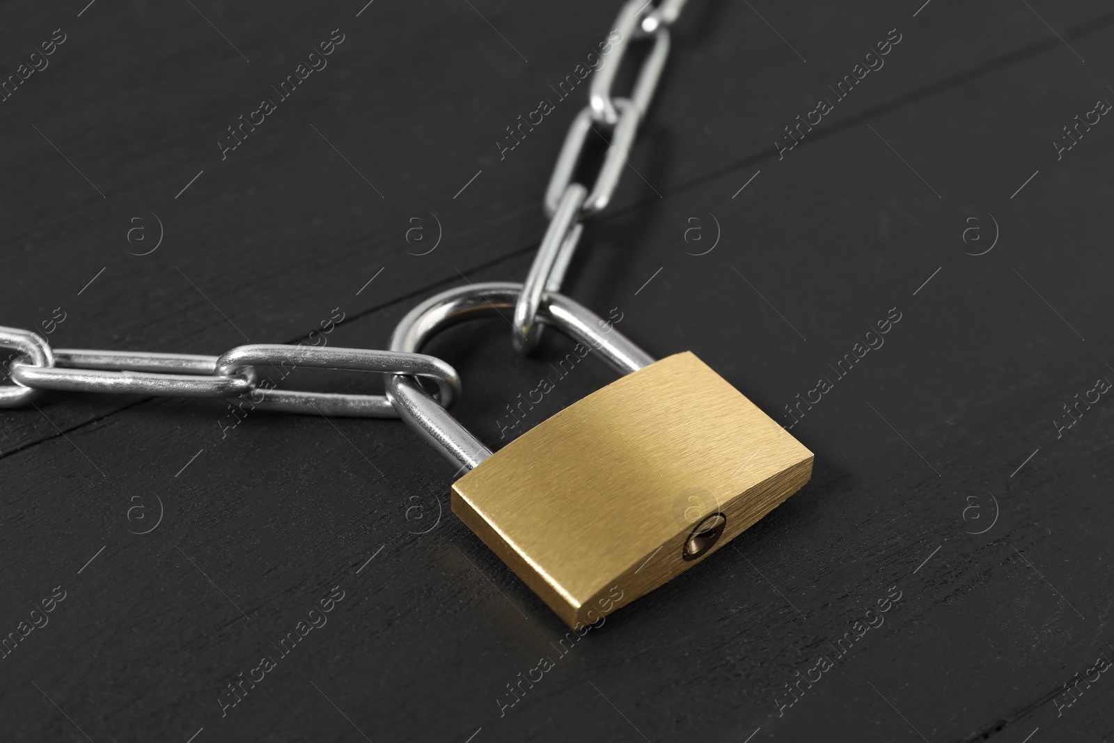 Photo of Steel padlock with chain on black wooden table, closeup