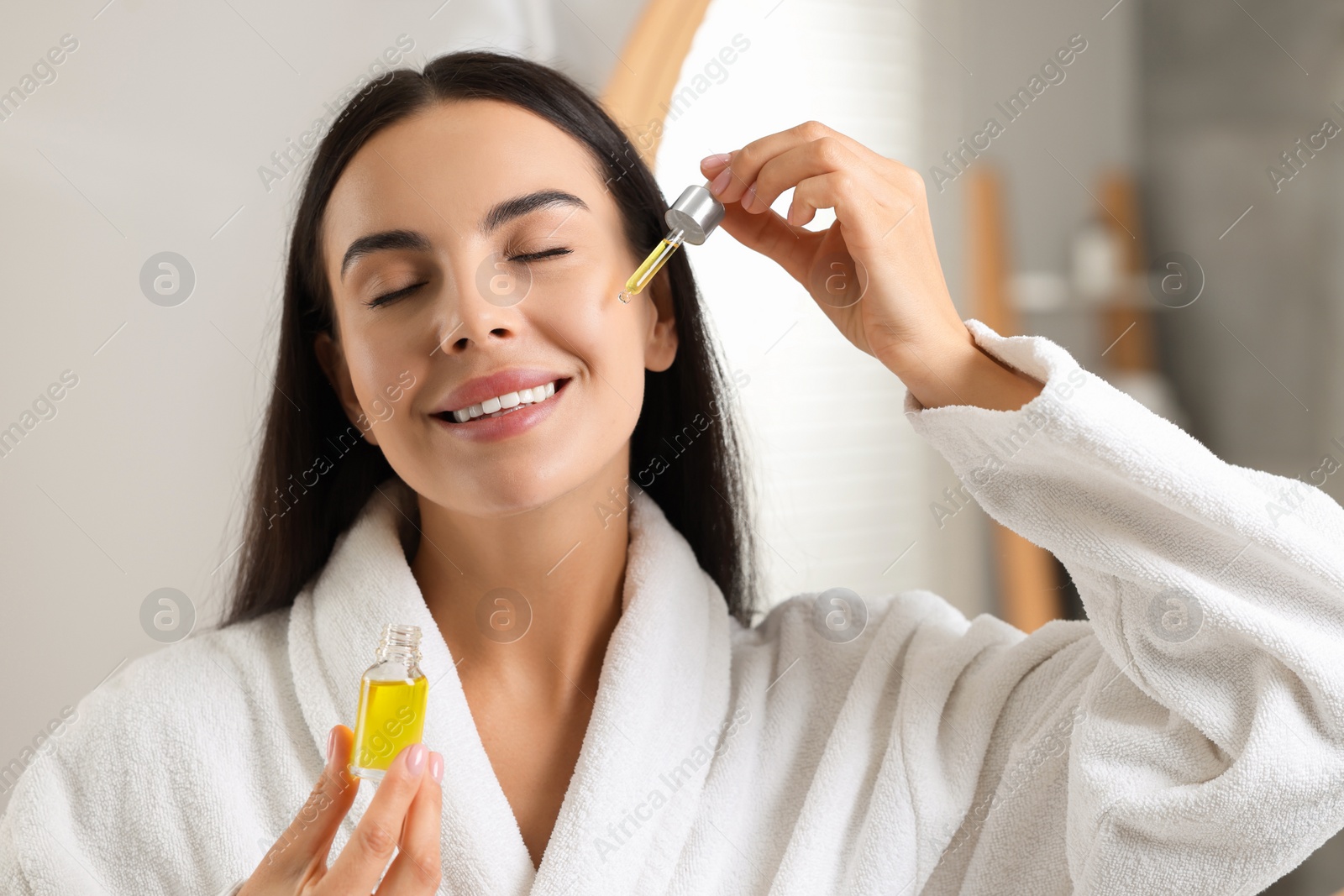 Photo of Beautiful young woman applying serum onto her face in bathroom
