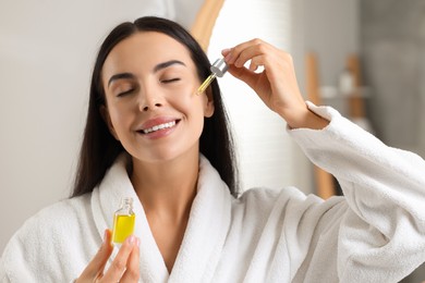 Beautiful young woman applying serum onto her face in bathroom