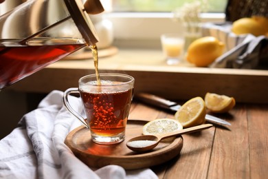 Photo of Pouring delicious tea into glass cup at wooden table, closeup. Space for text