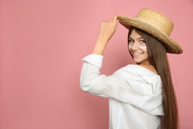 Teenage girl with sun protection cream on her face against pink background. Space for text