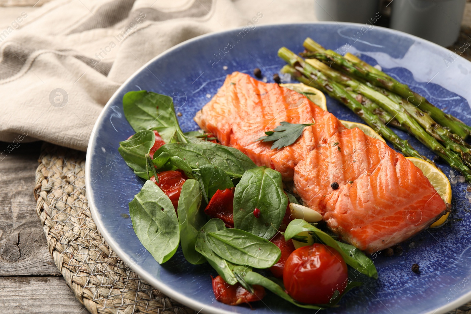 Photo of Tasty grilled salmon with tomatoes, asparagus, spinach and spices on table, closeup