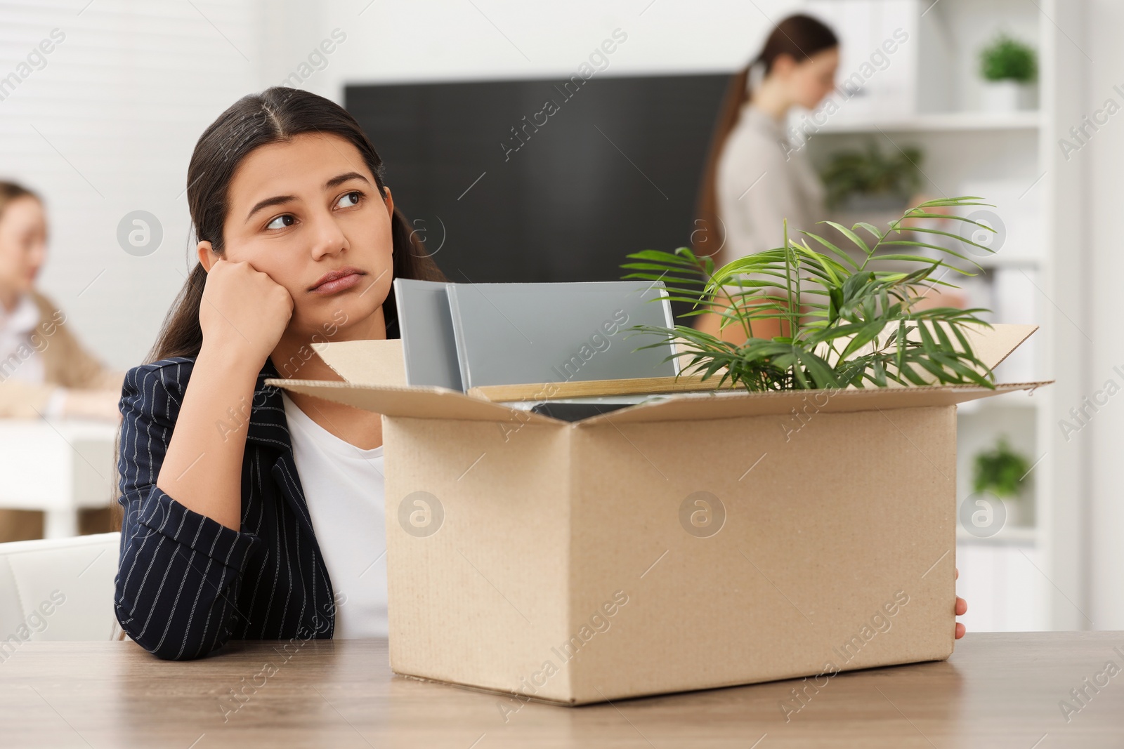 Photo of Unemployment problem. Woman with box of personal belongings at table in office