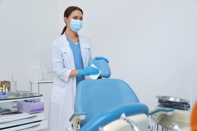 Photo of Professional dentist in white coat and medical mask cleaning workplace indoors