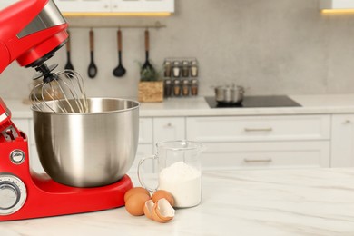 Modern red stand mixer, eggs and container with flour on white marble table in kitchen, space for text