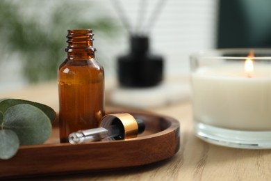 Photo of Aromatherapy. Bottle of essential oil and eucalyptus leaves on wooden table, closeup