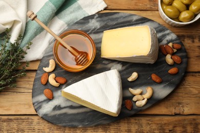 Photo of Tasty Camembert cheese with thyme, honey and nuts on wooden table, flat lay