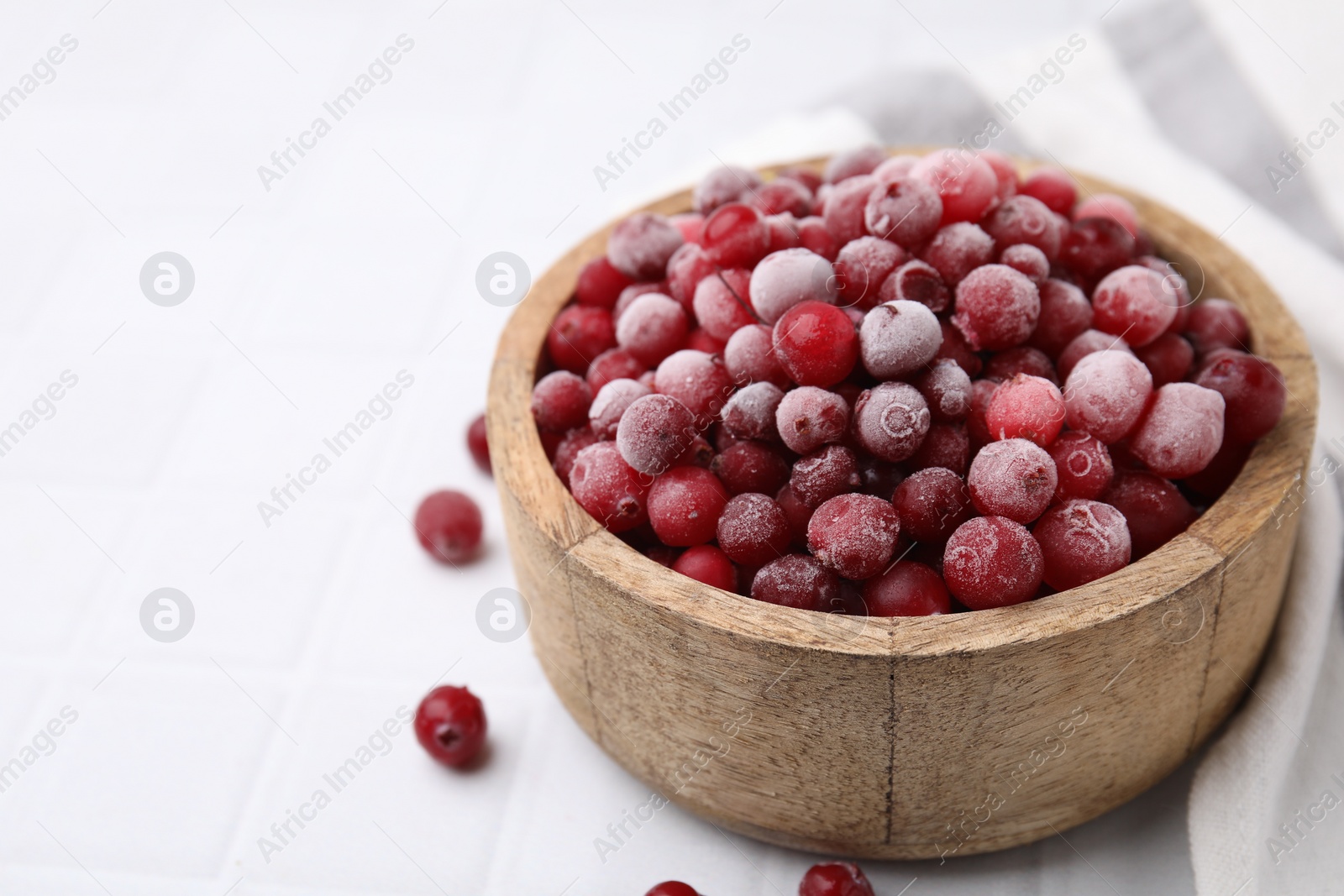 Photo of Frozen red cranberries in bowl on white tiled table, closeup. Space for text