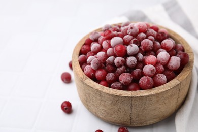 Photo of Frozen red cranberries in bowl on white tiled table, closeup. Space for text
