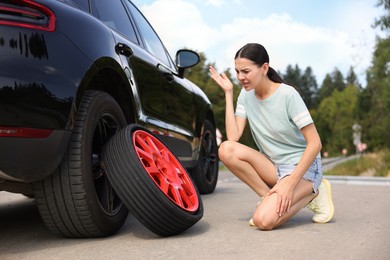 Photo of Tire puncture. Stressed woman with new wheel near car on roadside outdoors