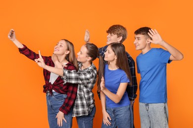 Group of happy teenagers taking selfie on orange background