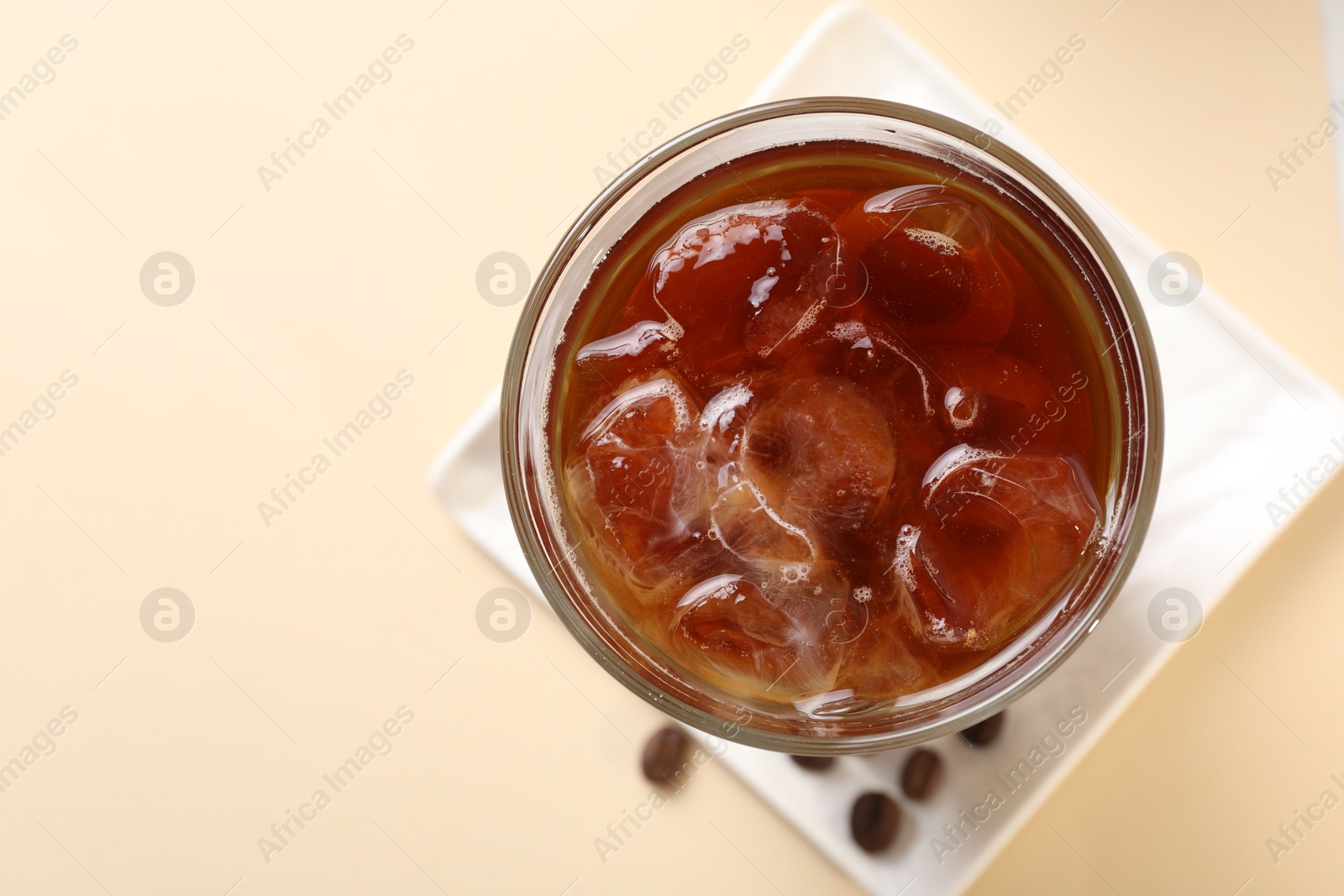 Photo of Refreshing iced coffee in glass on beige table, top view. Space for text