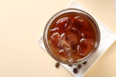 Photo of Refreshing iced coffee in glass on beige table, top view. Space for text